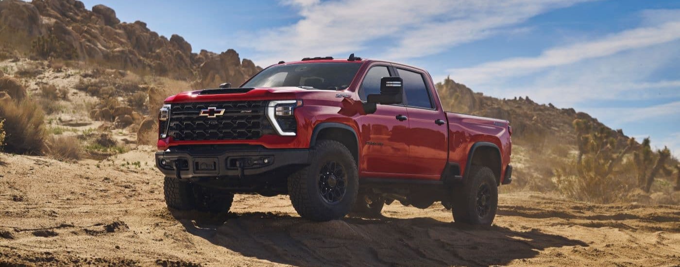 A red 2024 Chevy Silverado 2500 HD ZR2 Bison is shown from the front at an angle off-roading on a rocky trail.