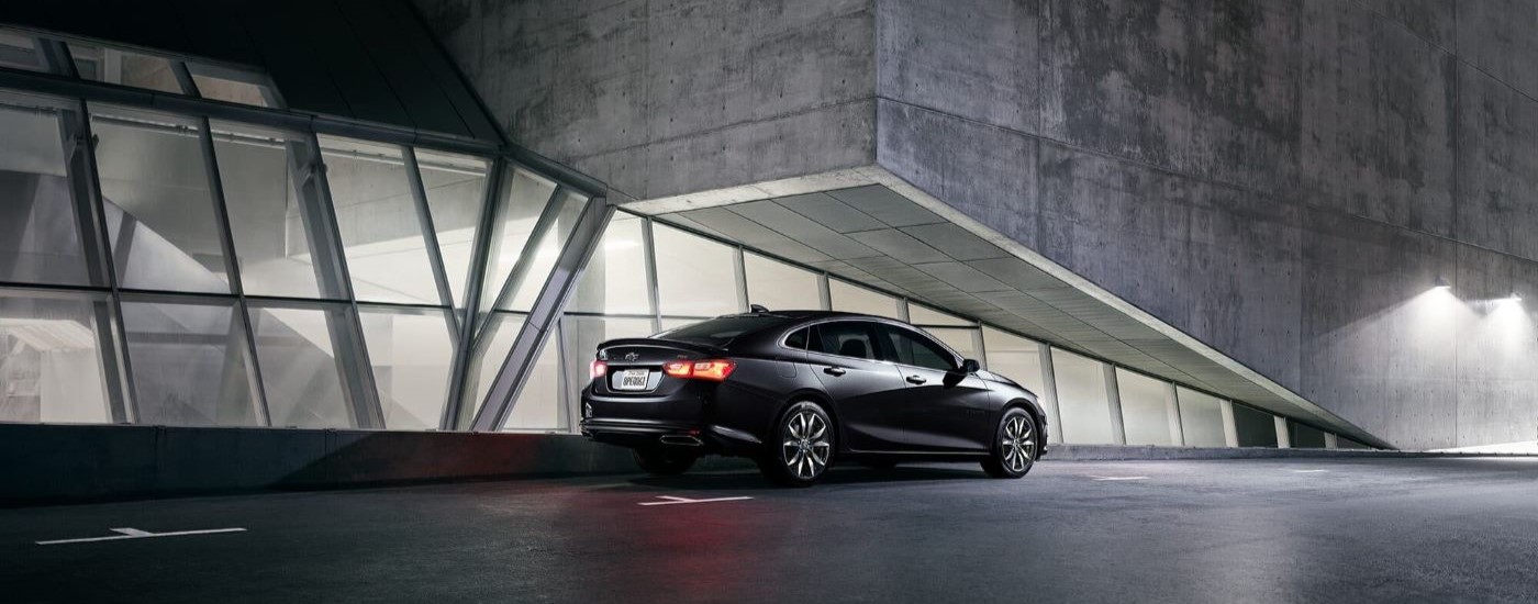 A black 2024 Chevy Malibu RS is parked at night near a Chevy dealer near Tomball.