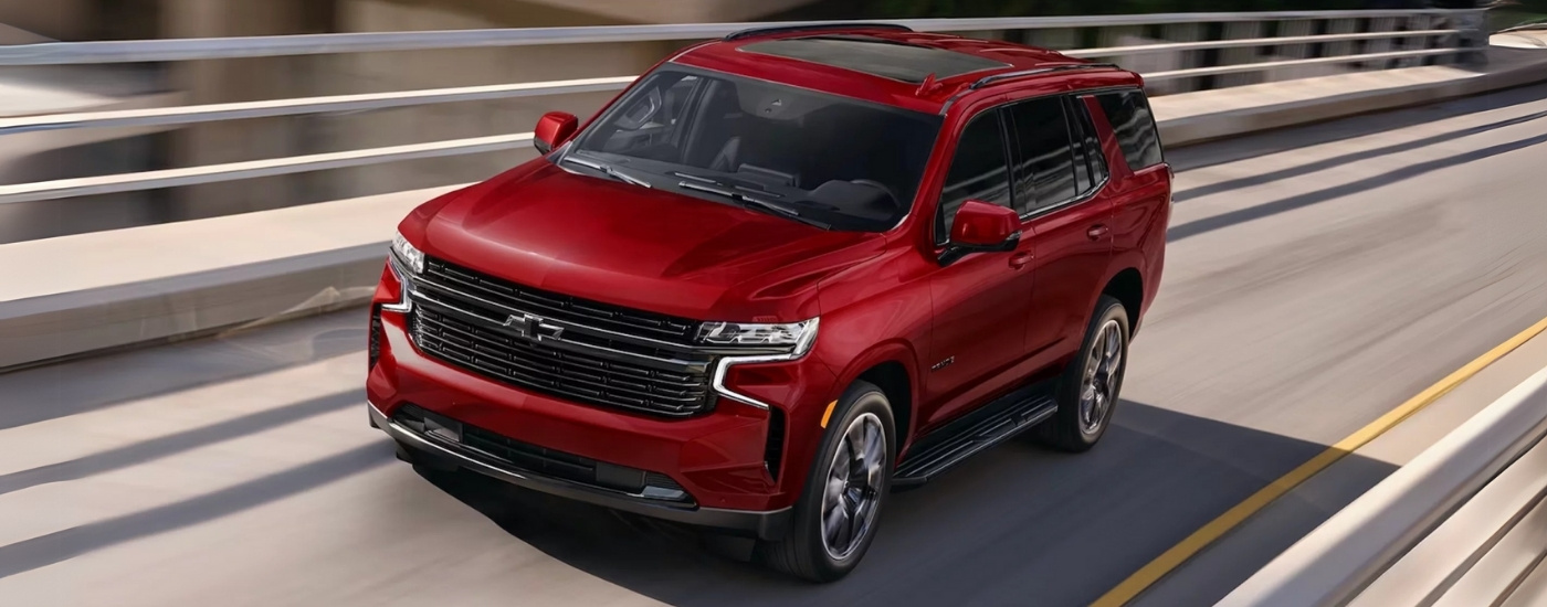 A red 2024 Chevy Tahoe RST is driving on a highway after leaving a Chevy dealer near Huntsville.