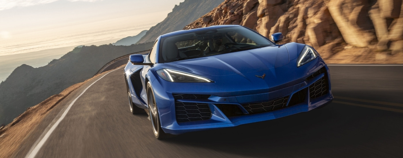 A blue 2024 Chevy Corvette E-Ray 3LZ is shown rounding a mountain corner.
