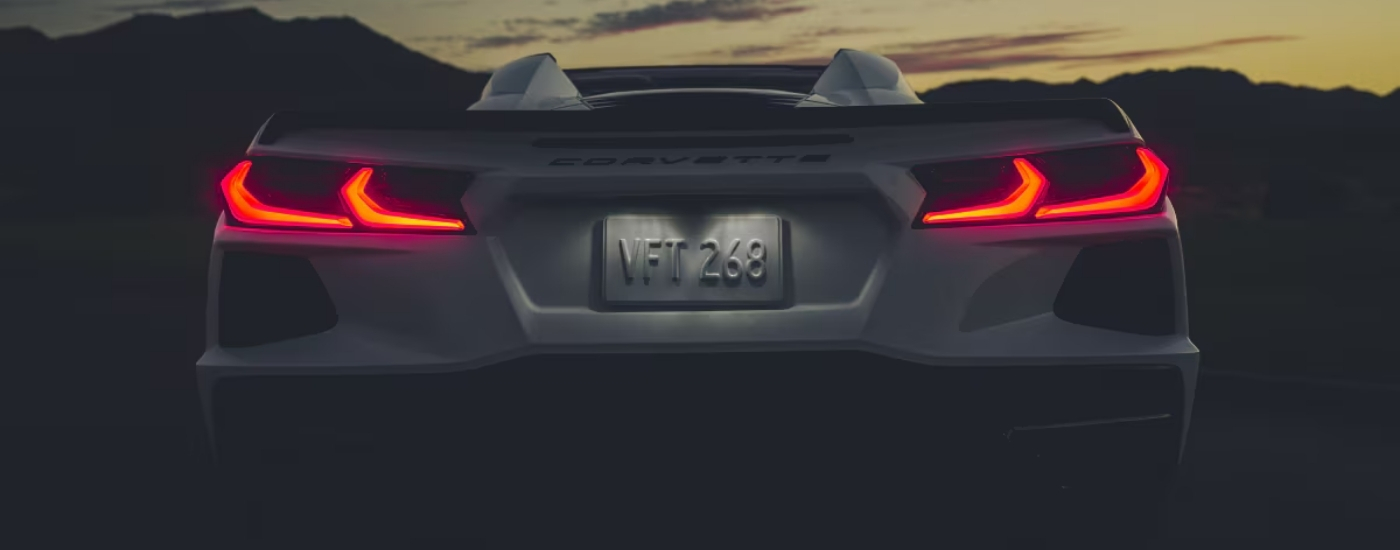 A close-up shows the illuminated taillights on a white 2025 Chevy Corvette Stingray at dusk.
