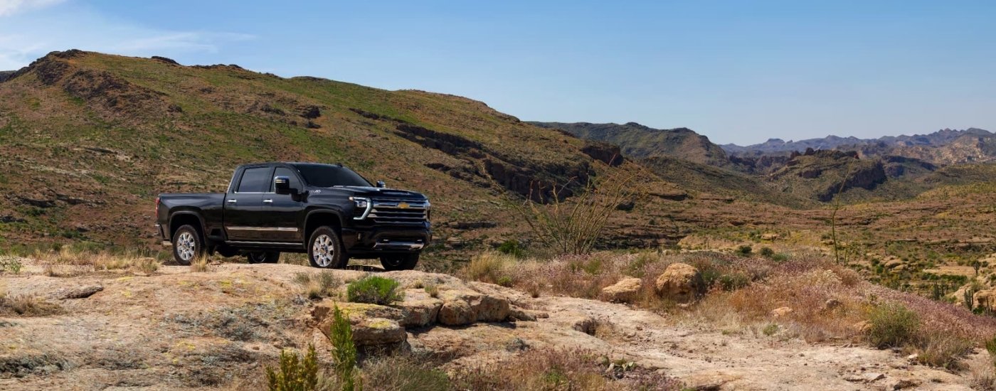 A black 2025 Chevy Silverado 2500 HD High Country is shown parked off-road.