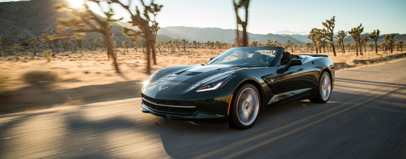 A popular used Chevy for sale, a black 2018 Chevy Corvette, is shown driving on an open road.