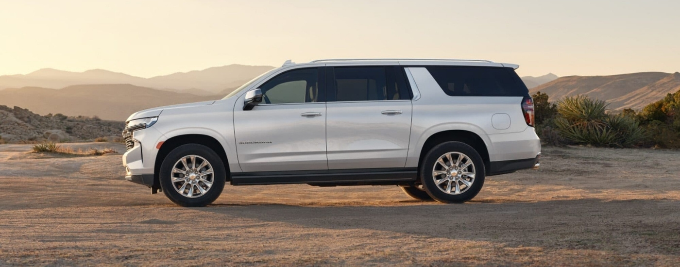 A white 2023 Chevy Suburban for sale is shown from the side at dusk.