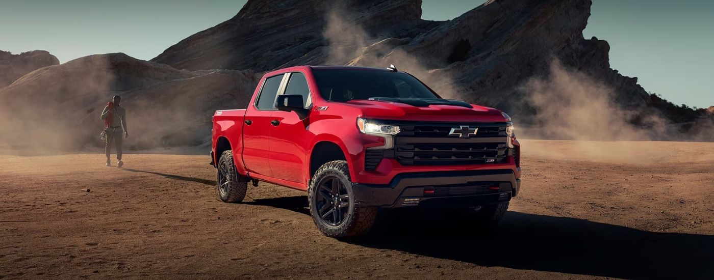 A red 2024 Chevy Silverado 1500 LT Trail Boss parked near a rocky outcropping.
