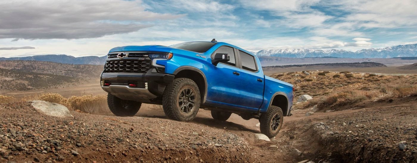 A low angle view of a white 2024 Chevy Silverado 1500 ZR2 parked off-road in a forest.