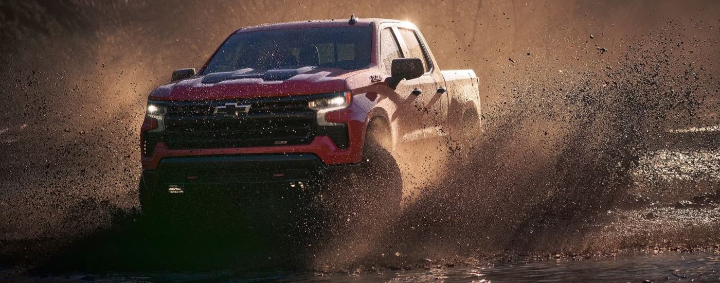 A red 2025 Chevy Silverado 1500 Z71 Trail Boss driving through a mud puddle.