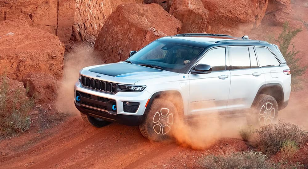 A silver and grey 2025 Jeep Grand Cherokee 4xe Trailhawk driving on a dusty trail.
