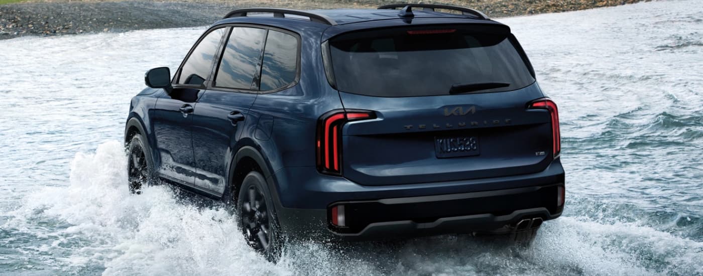 A blue 2025 Kia Telluride X-Pro is driving through a river.