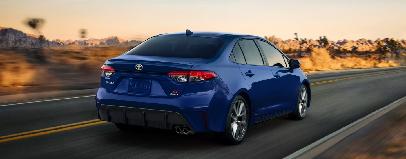 A blue 2023 Toyota Corolla SE driving to a used car dealer.