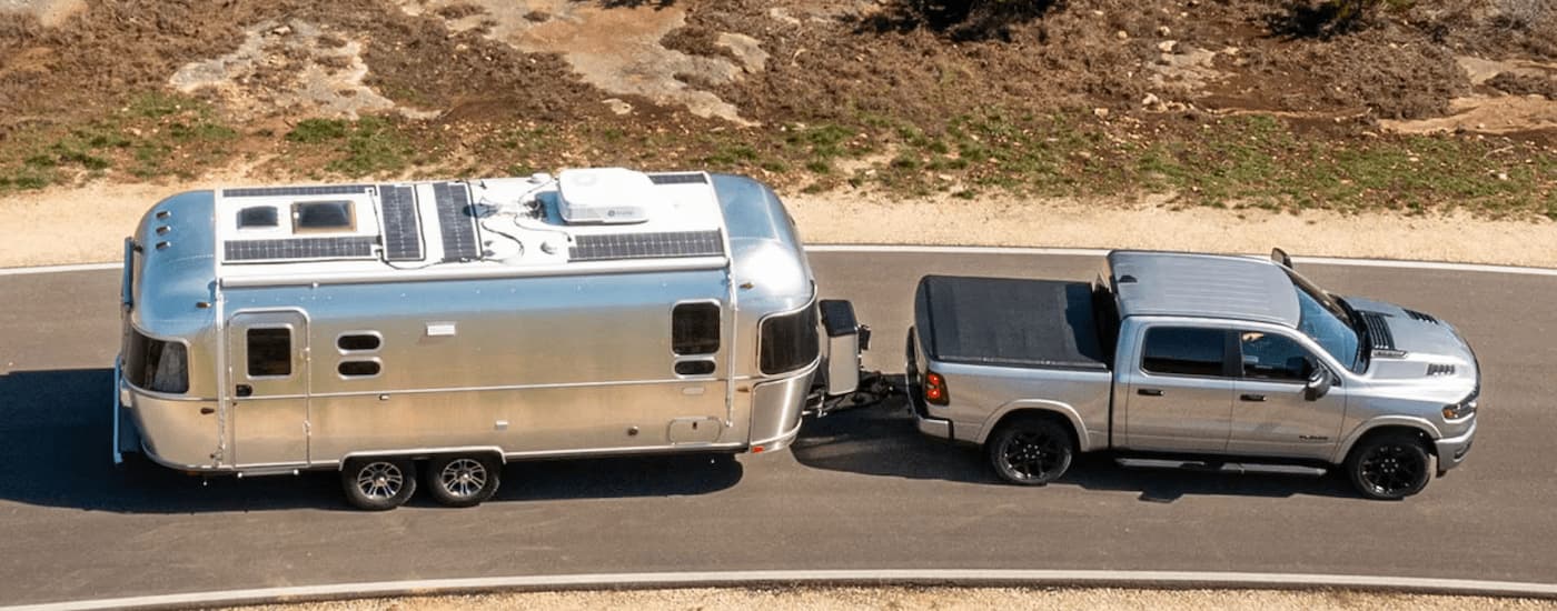 A silver 2025 Ram 1500 is towing an Airstream camper.