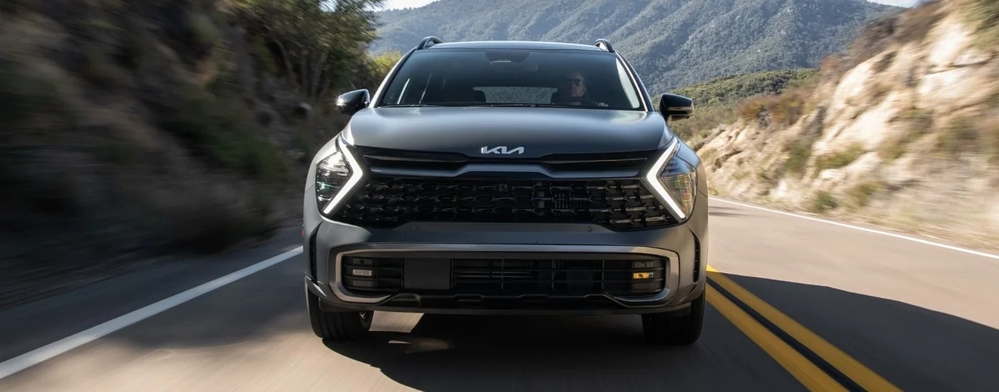 Front facing view of a grey 2025 Kia Sportage driving in the mountains.