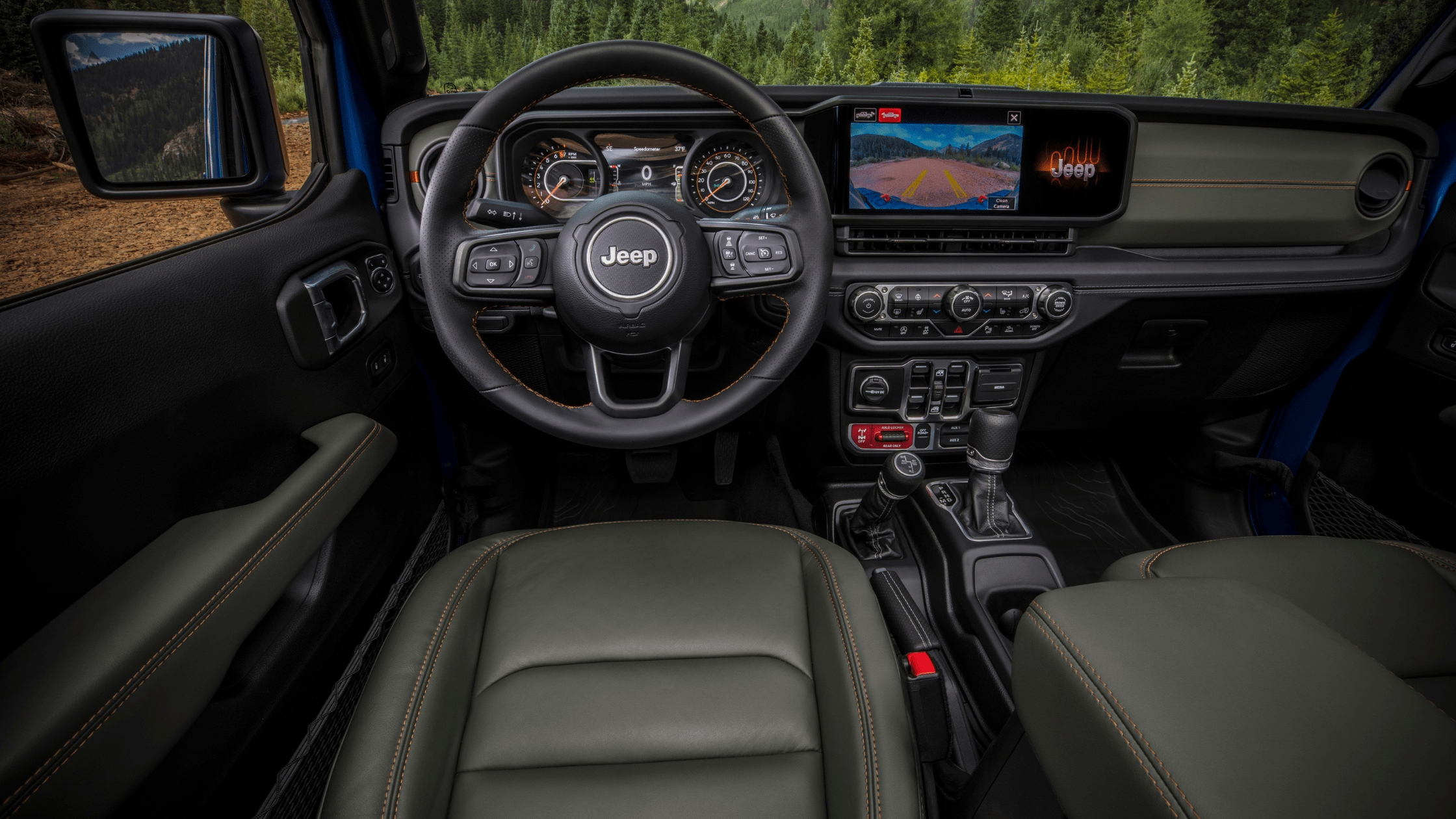 Interior view of the 2025 Jeep&reg; Gladiator featuring orange seat stitching, multifunction steering wheel, and center touchscreen displaying rearview camera.