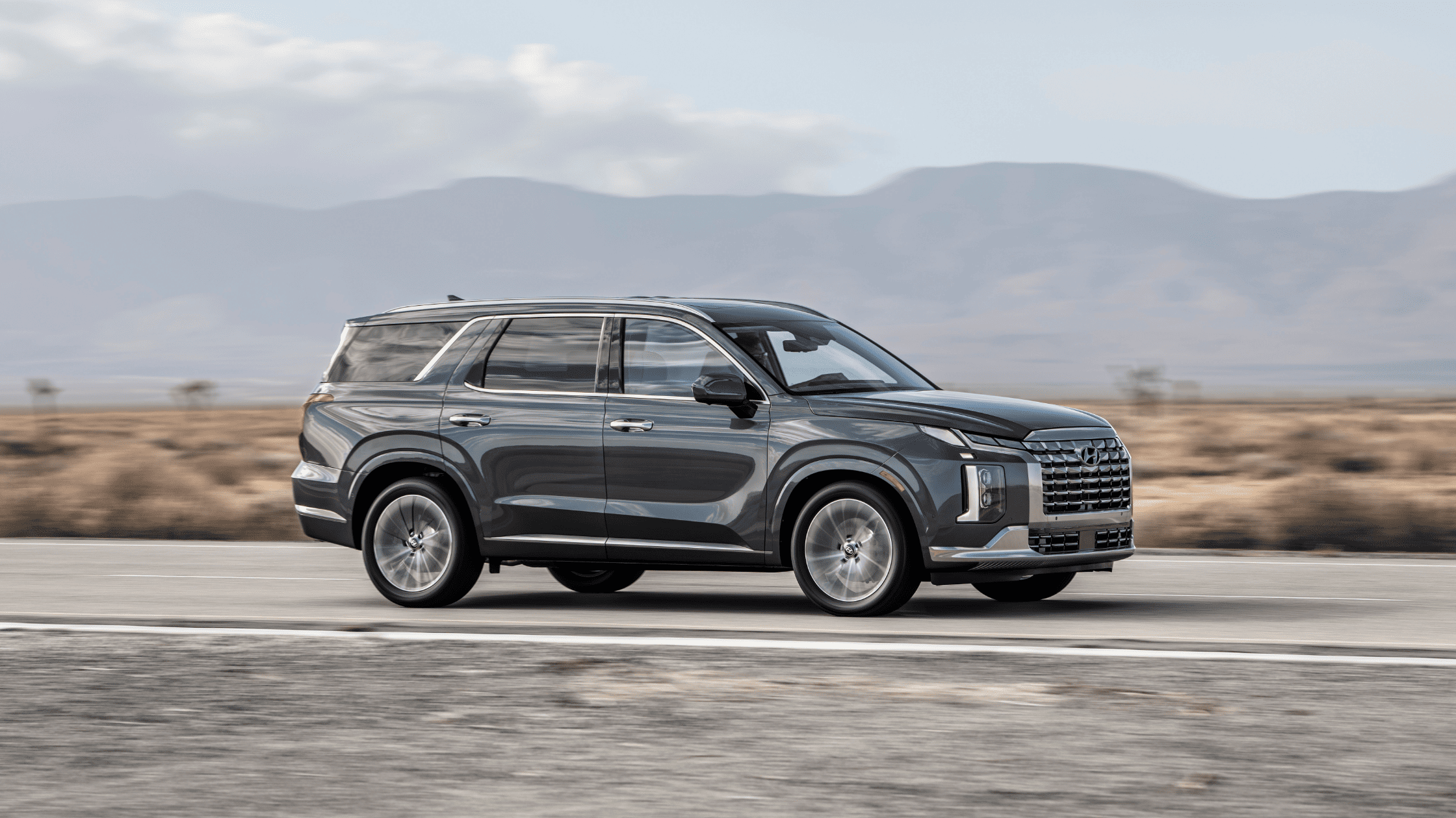 2025 Hyundai Palisade driving on open road, showcasing side profile and bold front grille