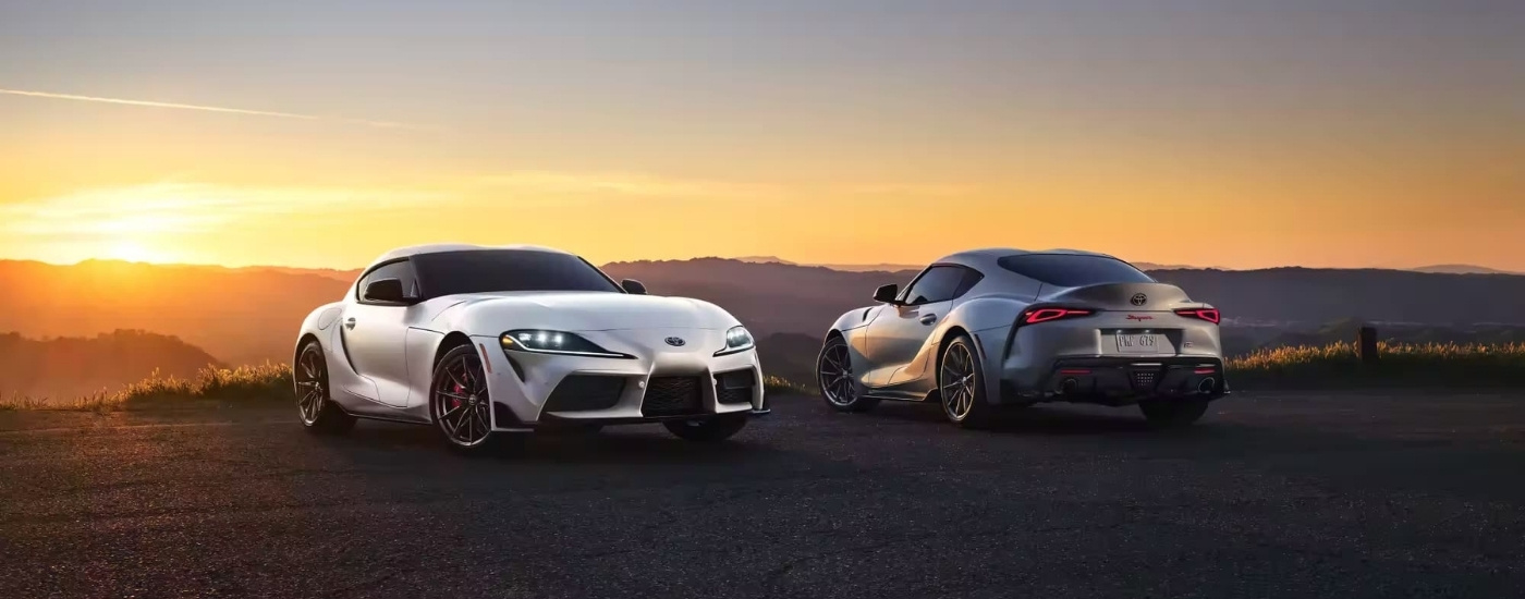 A white and a silver 2023 Toyota GR Supra are parked at sunrise.
