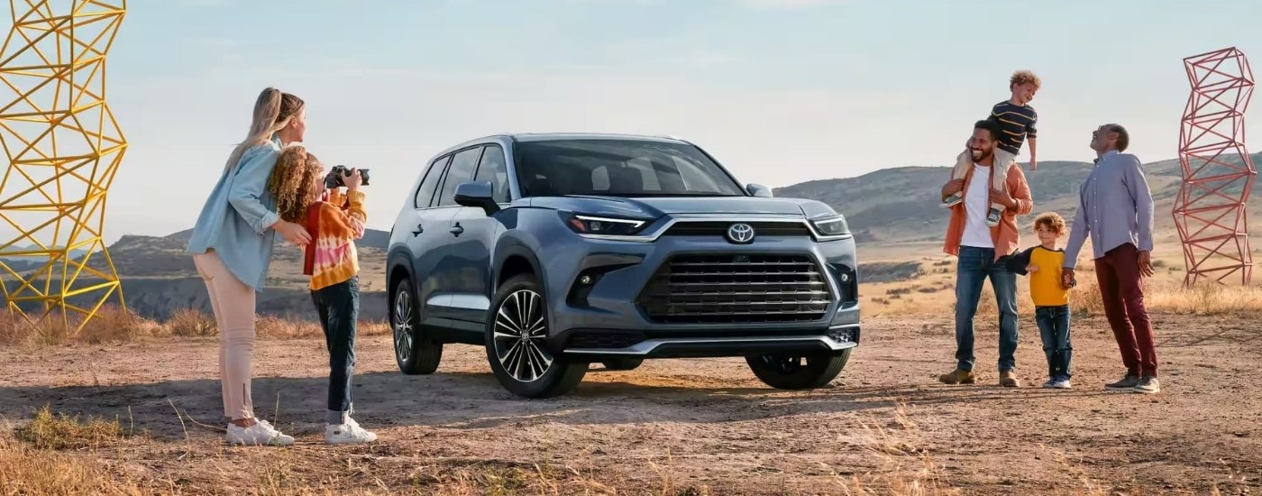 A family is talking a photo near a blue 2024 Toyota Grand Highlander Platinum MAX.