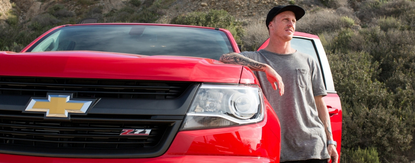 A person is leaning against a red 2015 Chevy Colorado for sale near Cypress.