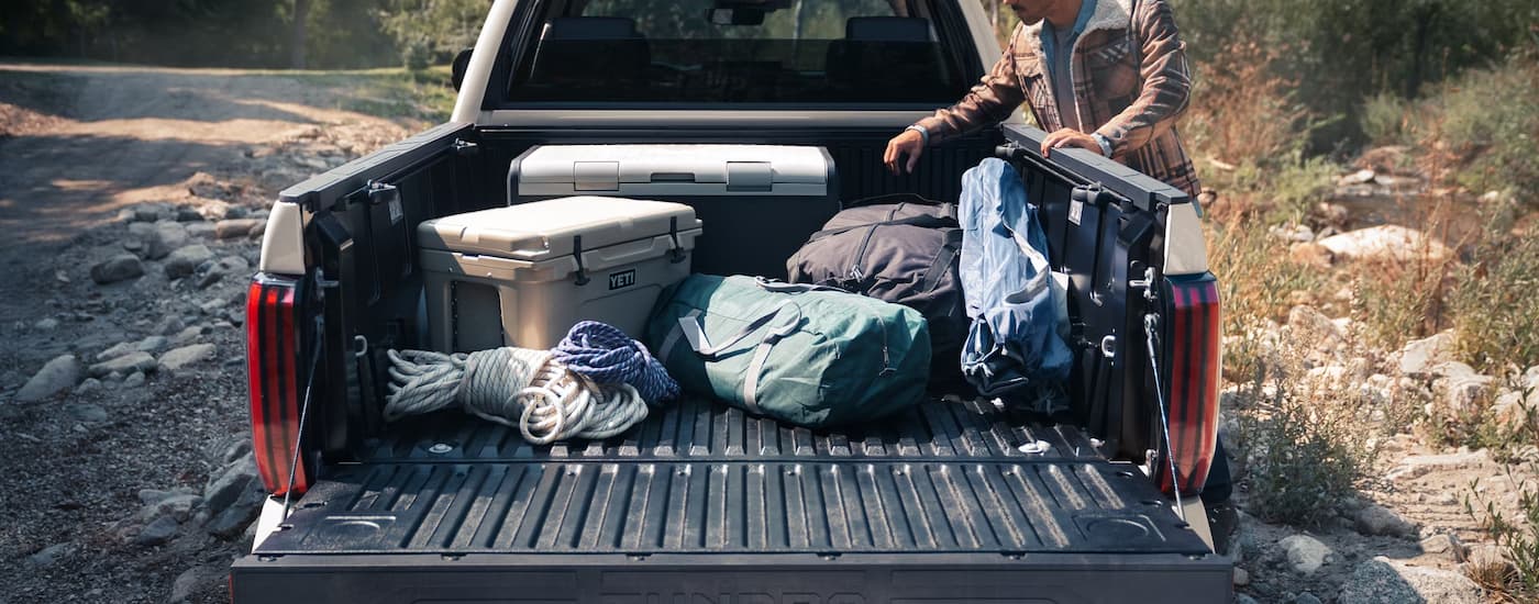 Man getting camping supplies out of the bed of a white 2025 Toyota Tundra.