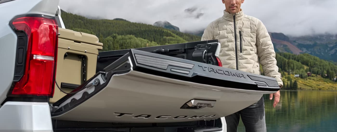 Man lowering the tailgate on a white 2025 Toyota Tacoma.
