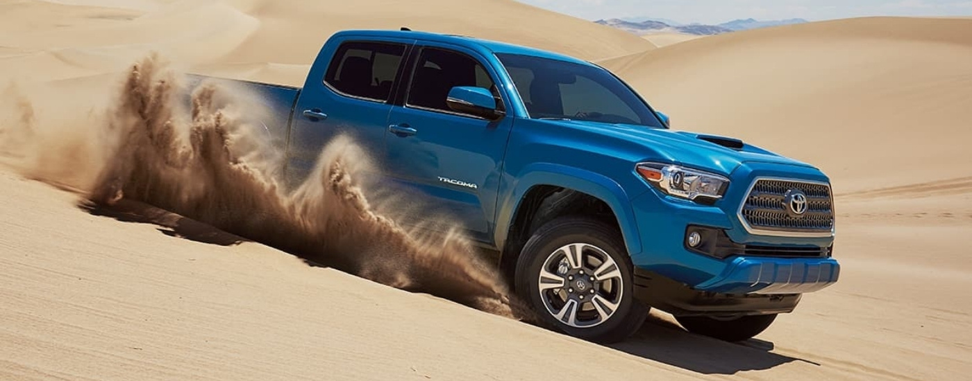 A blue 2016 Toyota Tacoma driving to look at used trucks for sale.