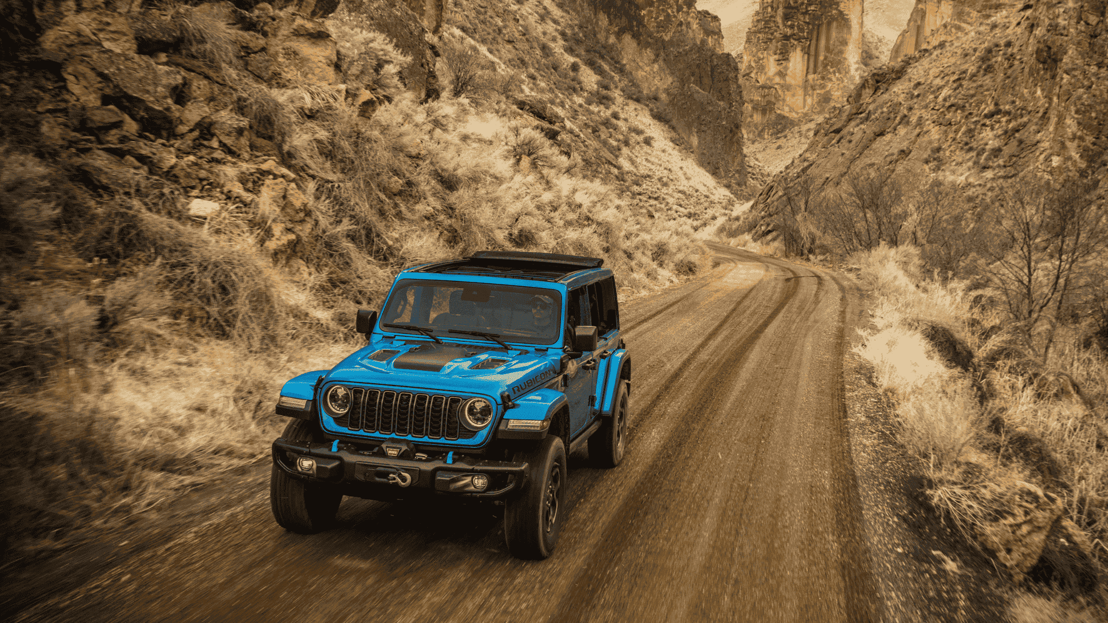 Blue 2025 Jeep Wrangler 4xe navigating rugged terrain with lifted suspension.