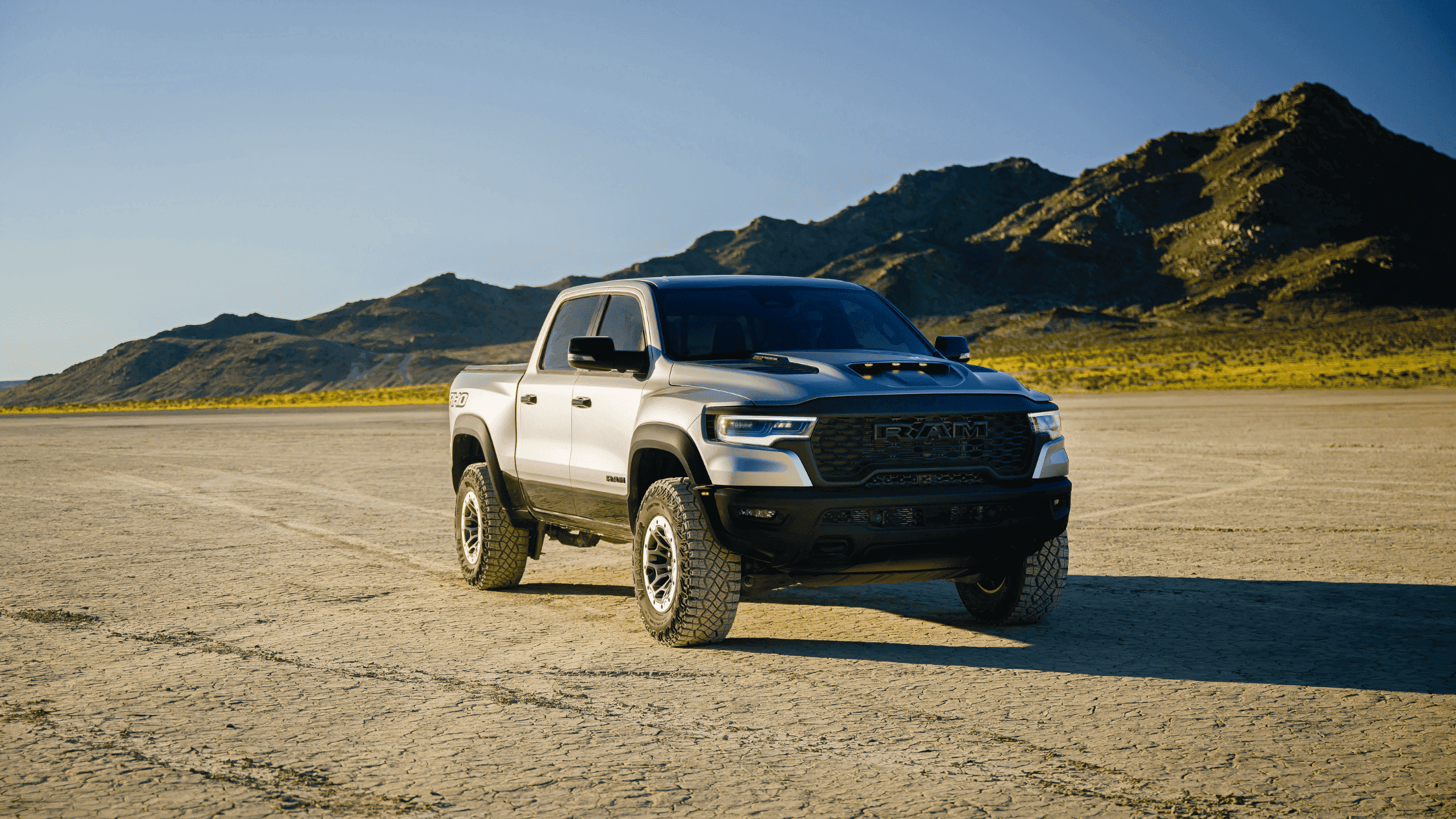Silver 2025 Ram 1500 RHO parked on dry terrain with mountains in the background.