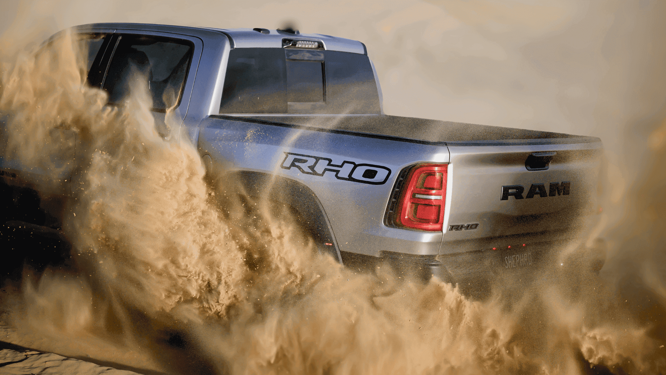 Ram 1500 RHO kicking up desert sand, showcasing off-road power and traction control.