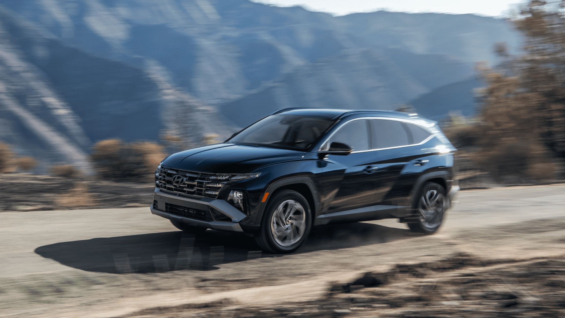 2025 Hyundai Tucson Hybrid in black driving along a mountain road at high speed