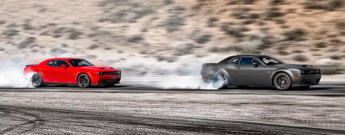A red and a grey 2023 Dodge Challenger doing a burnout.