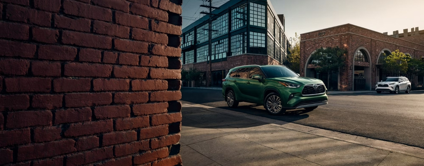 A green 2025 Toyota Highlander from the side on a city street.