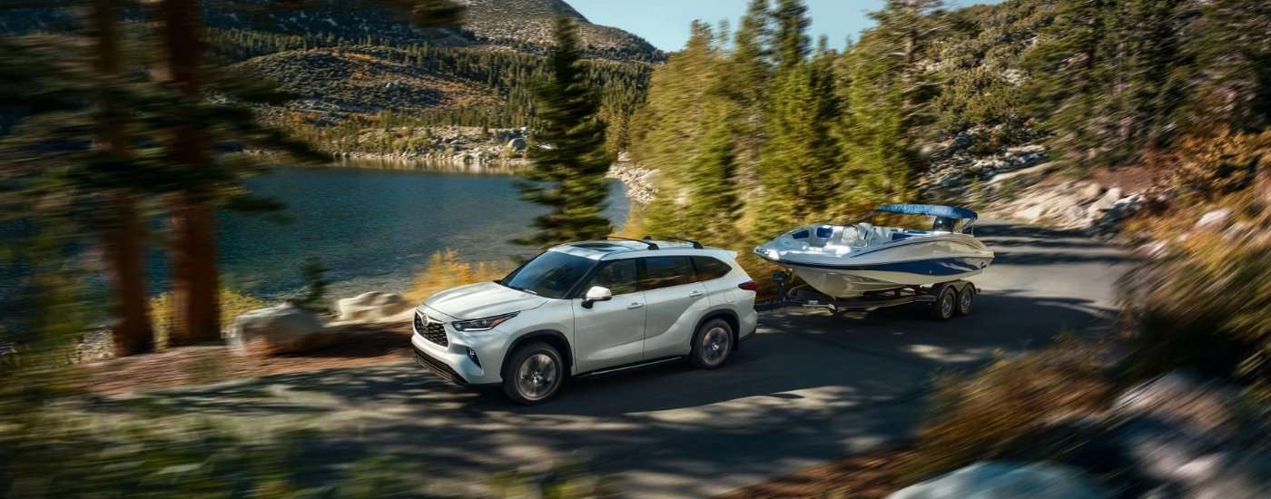 A white 2025 Toyota Highlander from the side while towing a boat.