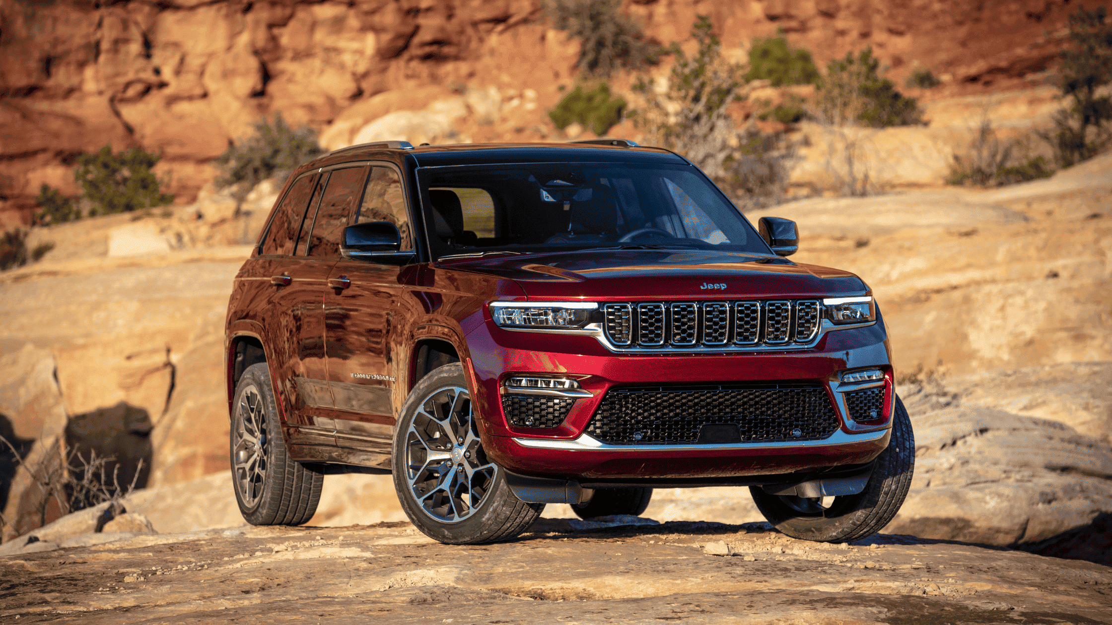 2025 Jeep Grand Cherokee in red parked on rocky terrain with desert cliffs in background