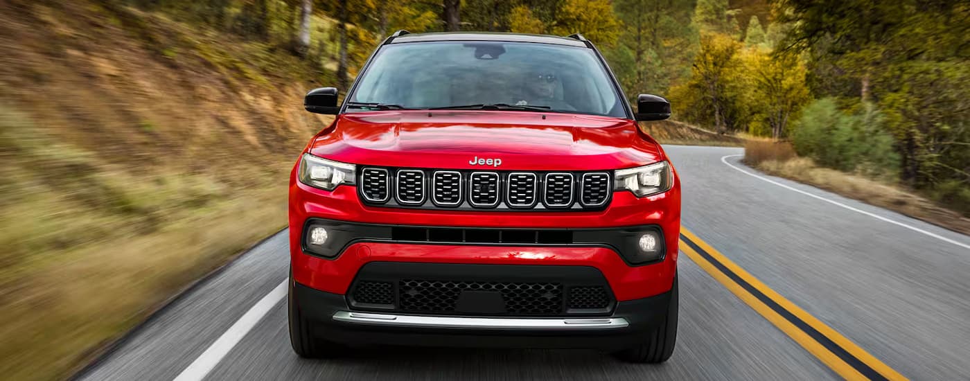 Red 2025 Jeep Compass driving on a tree-lined road.