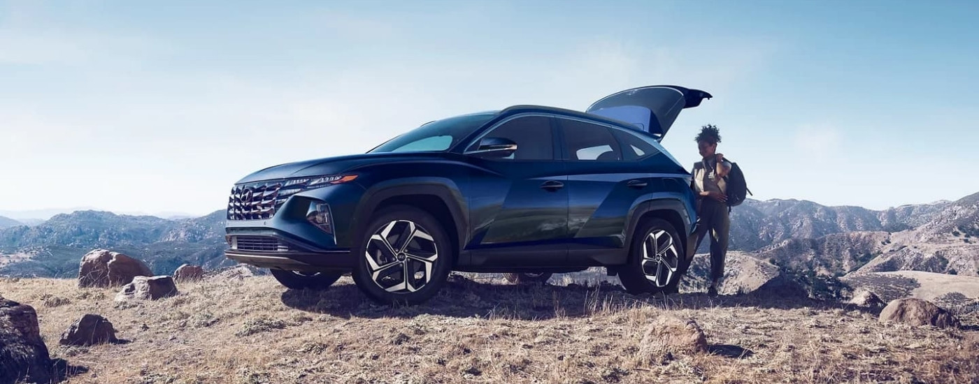 A hiker near a dark blue 2023 Hyundai Tucson Hybrid.
