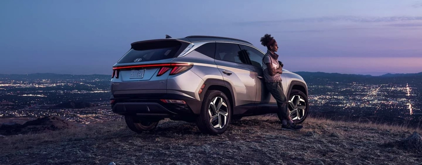 A person leaning against a silver 2023 Hyundai Tucson for sale.