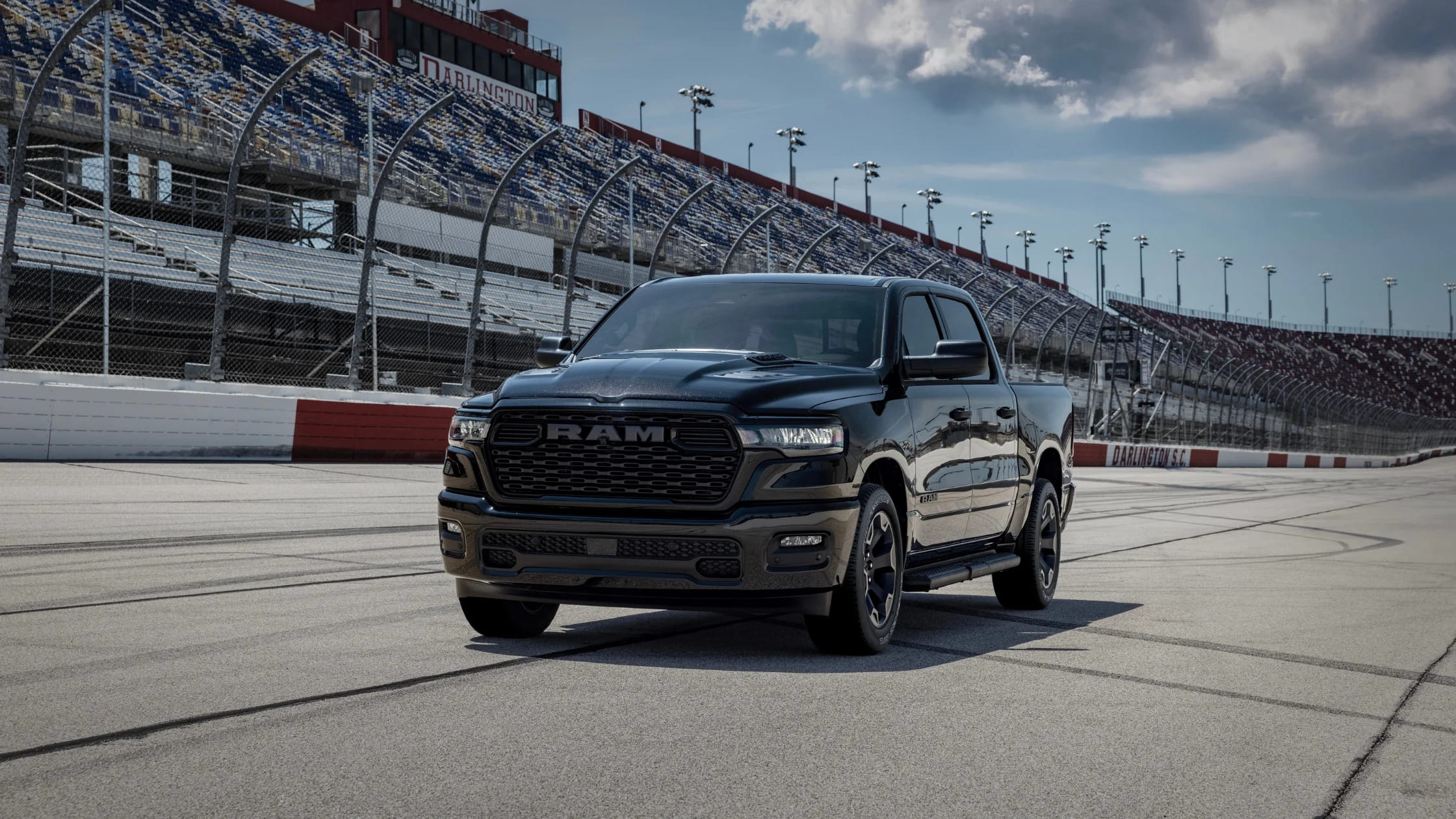 2026 Ram 1500 Express in black parked on racetrack with Darlington Raceway grandstand in background.