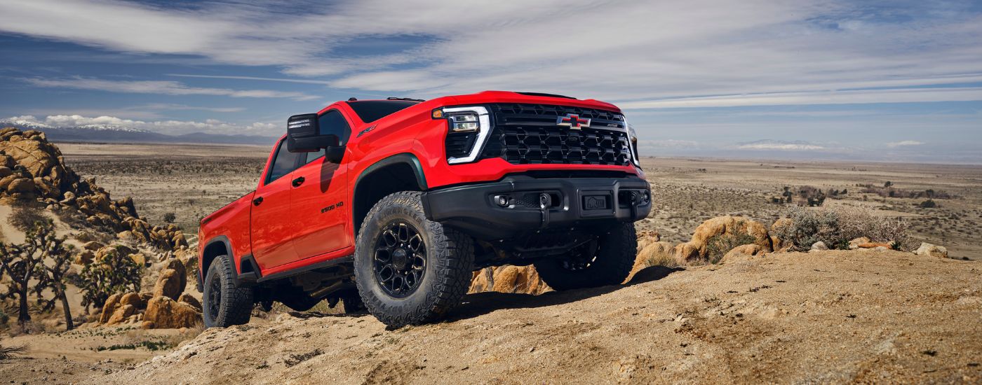 Red 2024 Chevy Silverado 2500HD driving on dirt.