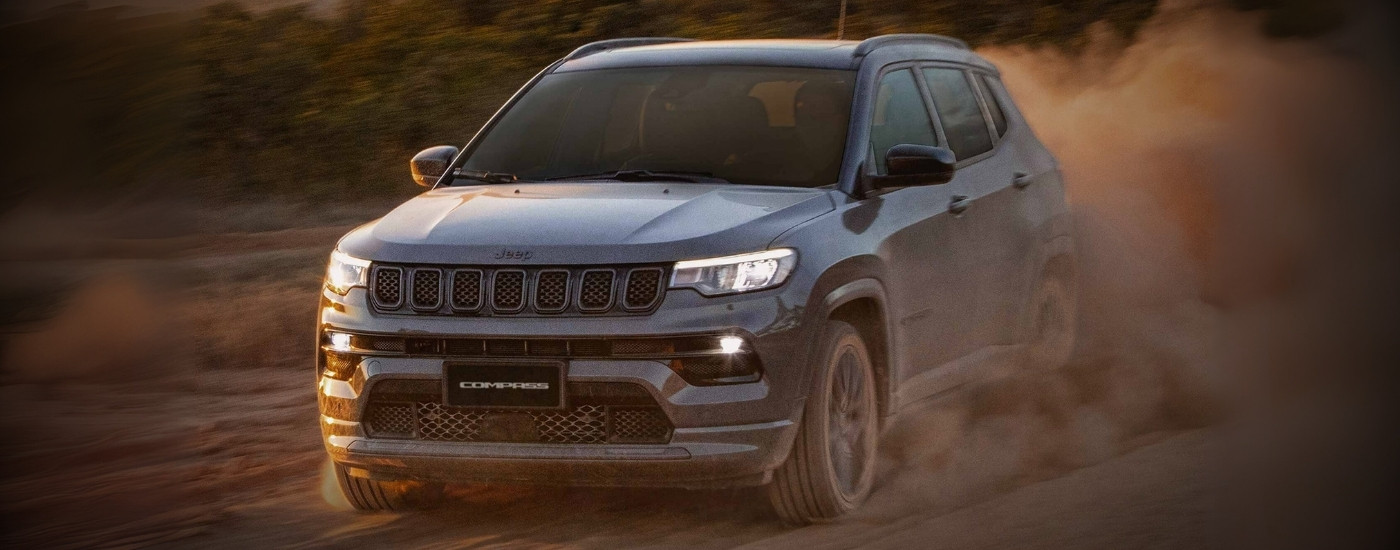 A grey 2025 Jeep Compass for sale near Katy kicking up dust off-road.