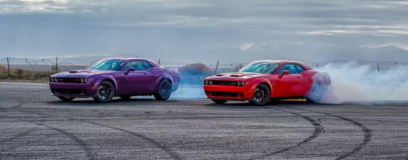 A purple 2023 Dodge Challenger RT and red Challenger SRT drifting in tandem.