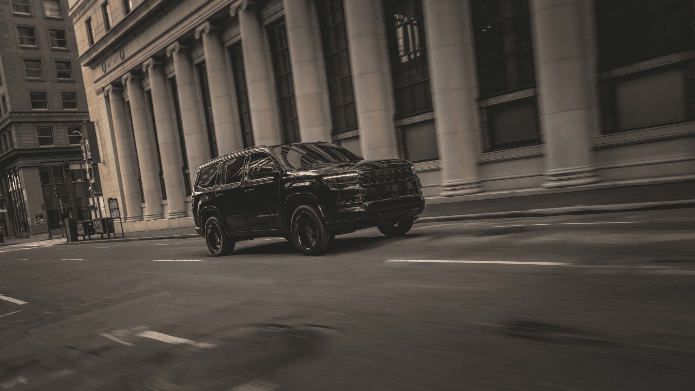 2025 Jeep Grand Wagoneer in black driving past urban architecture in a downtown setting