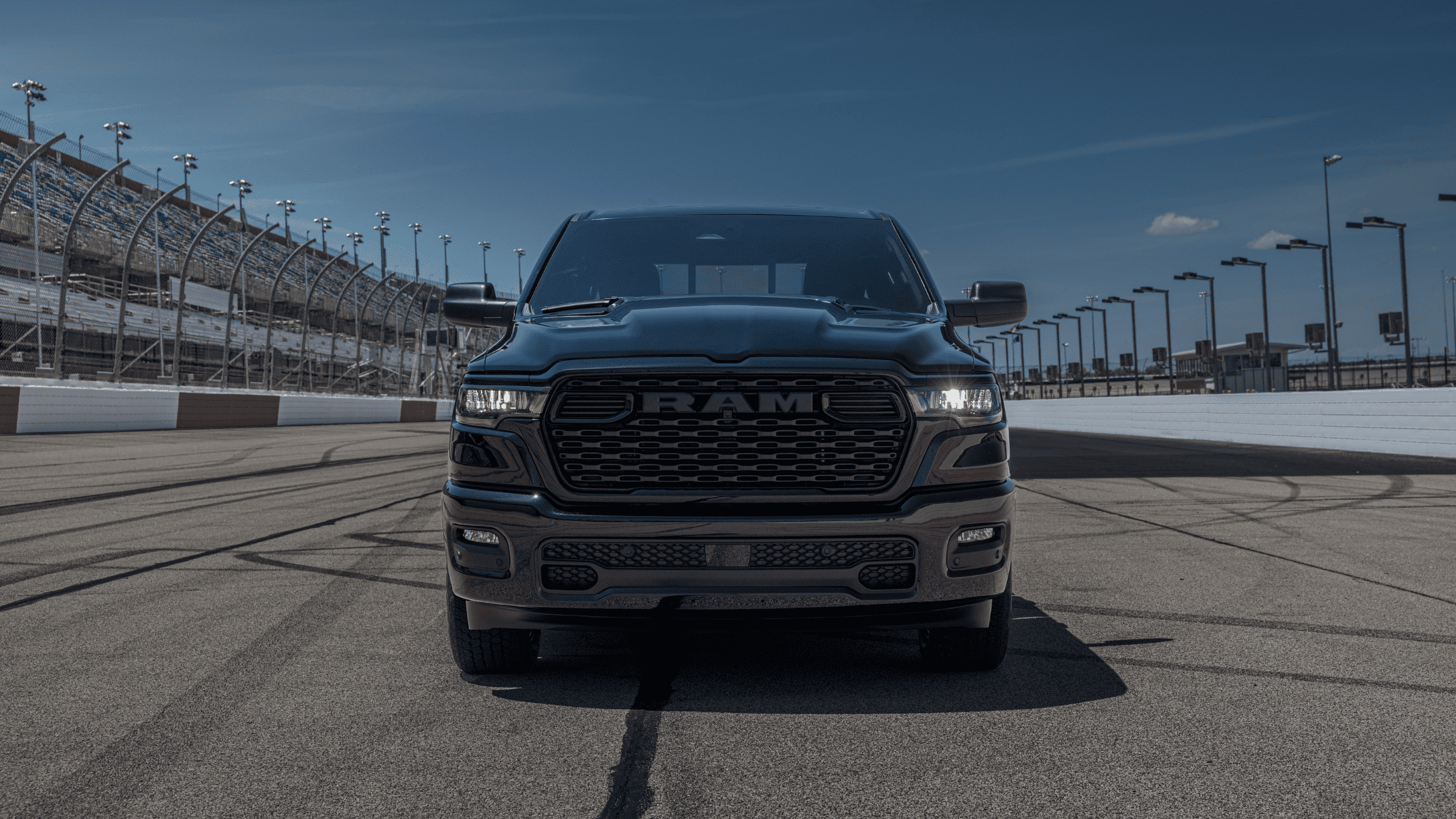 Front view of 2026 Ram 1500 Express in black parked on a racetrack with grandstands in background.