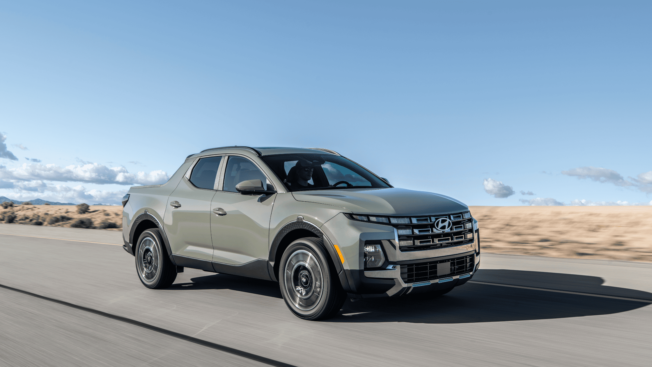 2025 Hyundai Santa Cruz pickup driving on highway with desert landscape and clear blue sky.