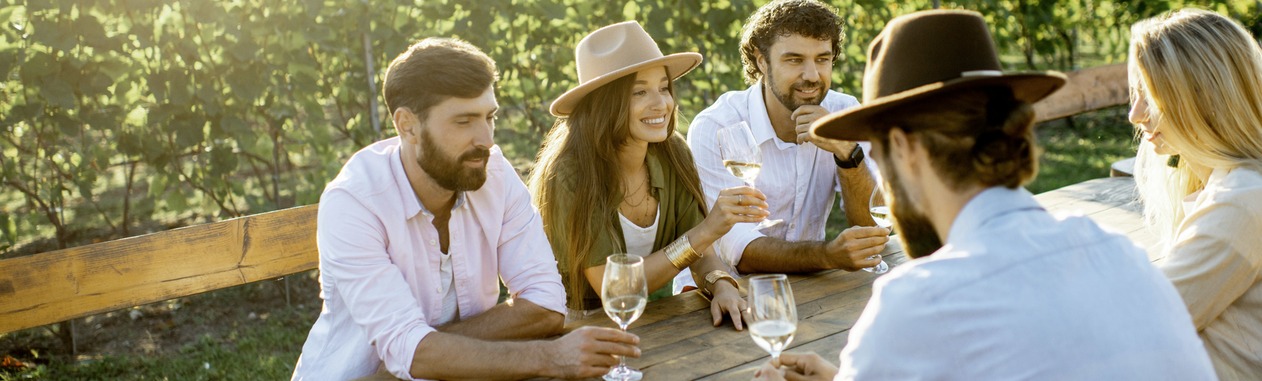 a friend group sitting and drinking wine together at a vineyard