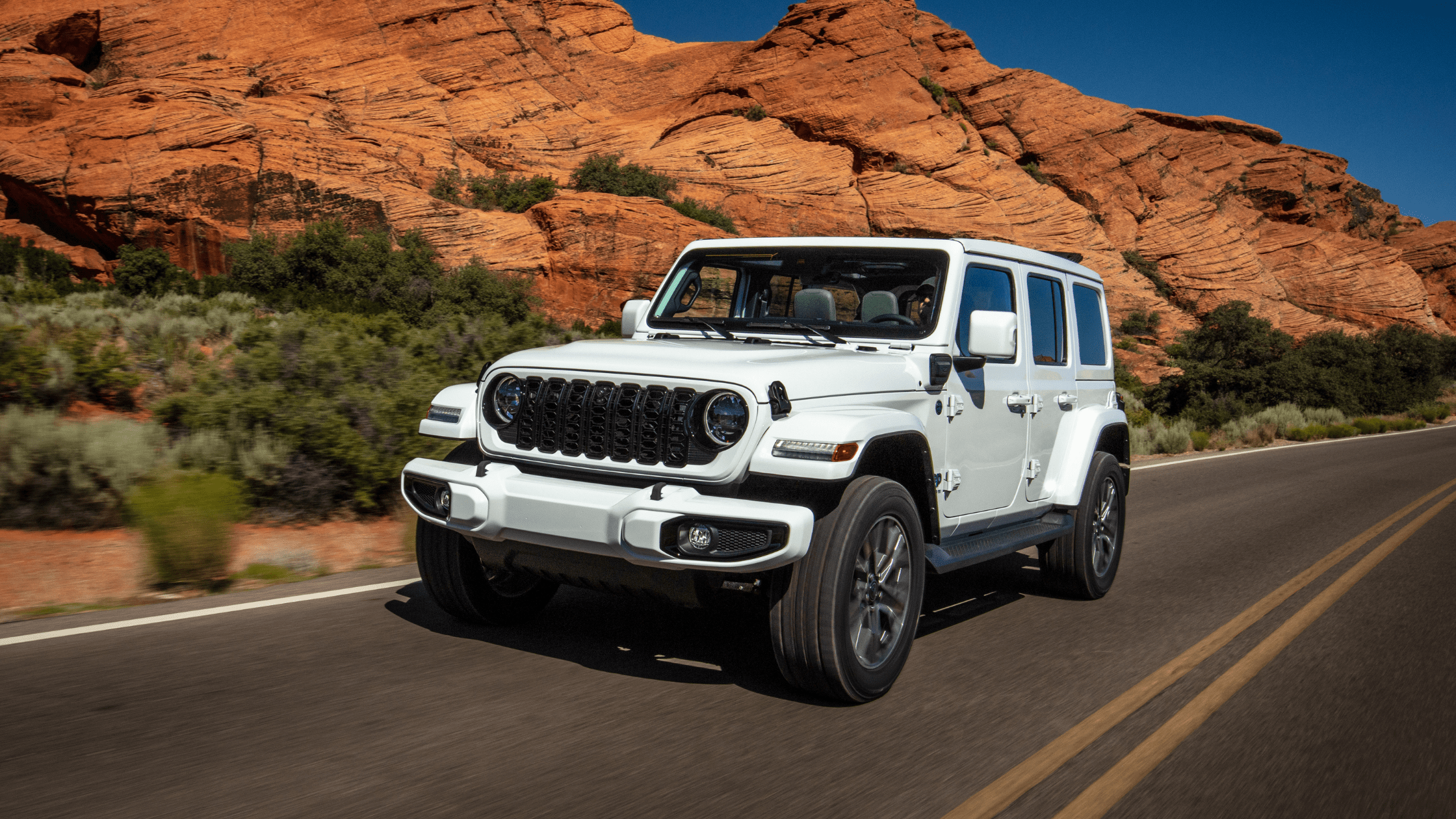 2025 Jeep Wrangler 4xe in white driving through scenic red rock desert highway.