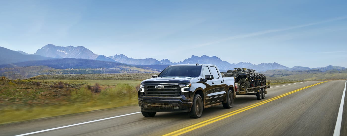 Black 2025 Chevy Silverado 1500 High Country towing ATVs on a trailer