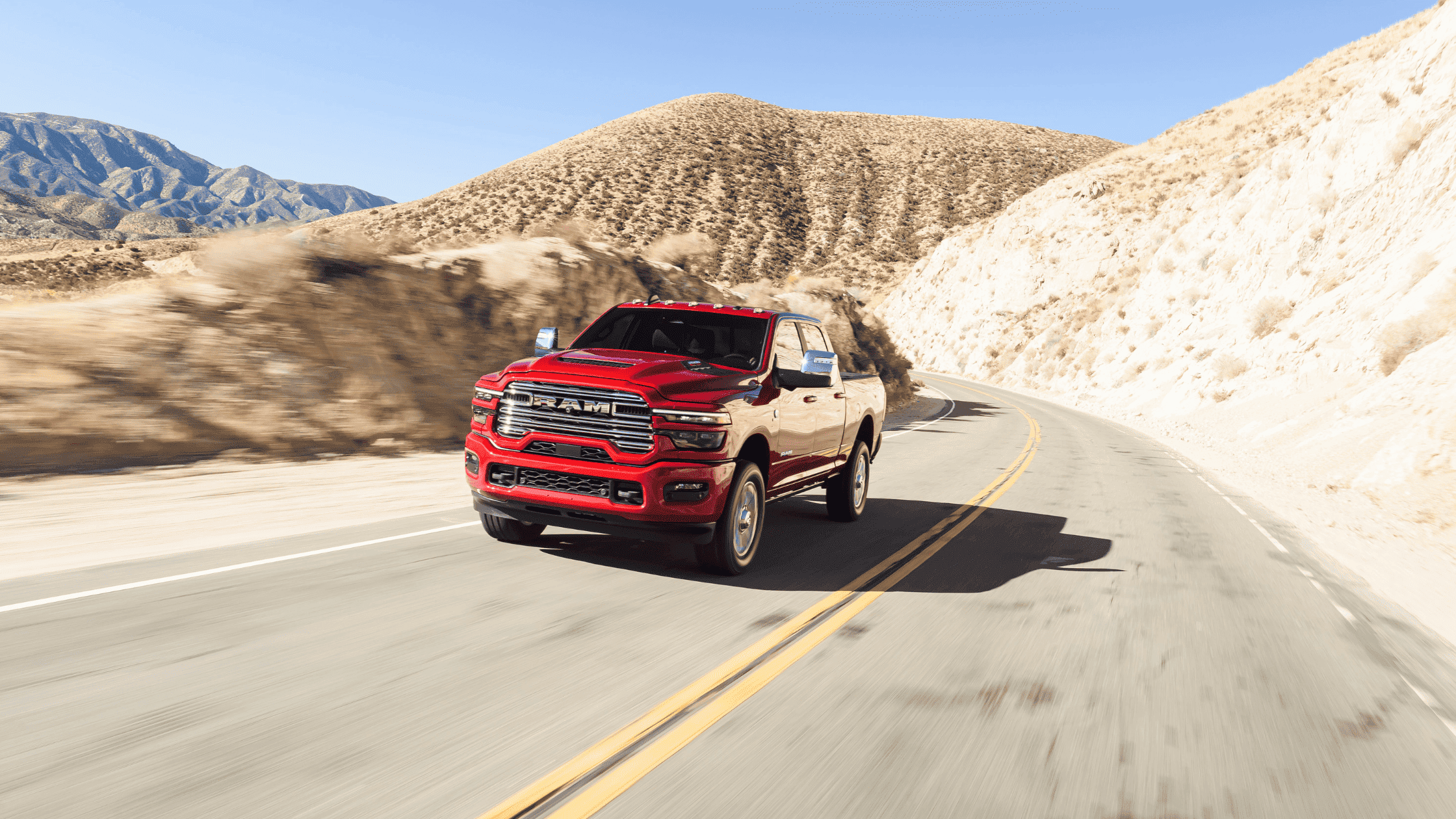 Red 2025 Ram 2500 heavy-duty truck cruising on a desert highway, bold grille and rugged body highlighted in daylight.
