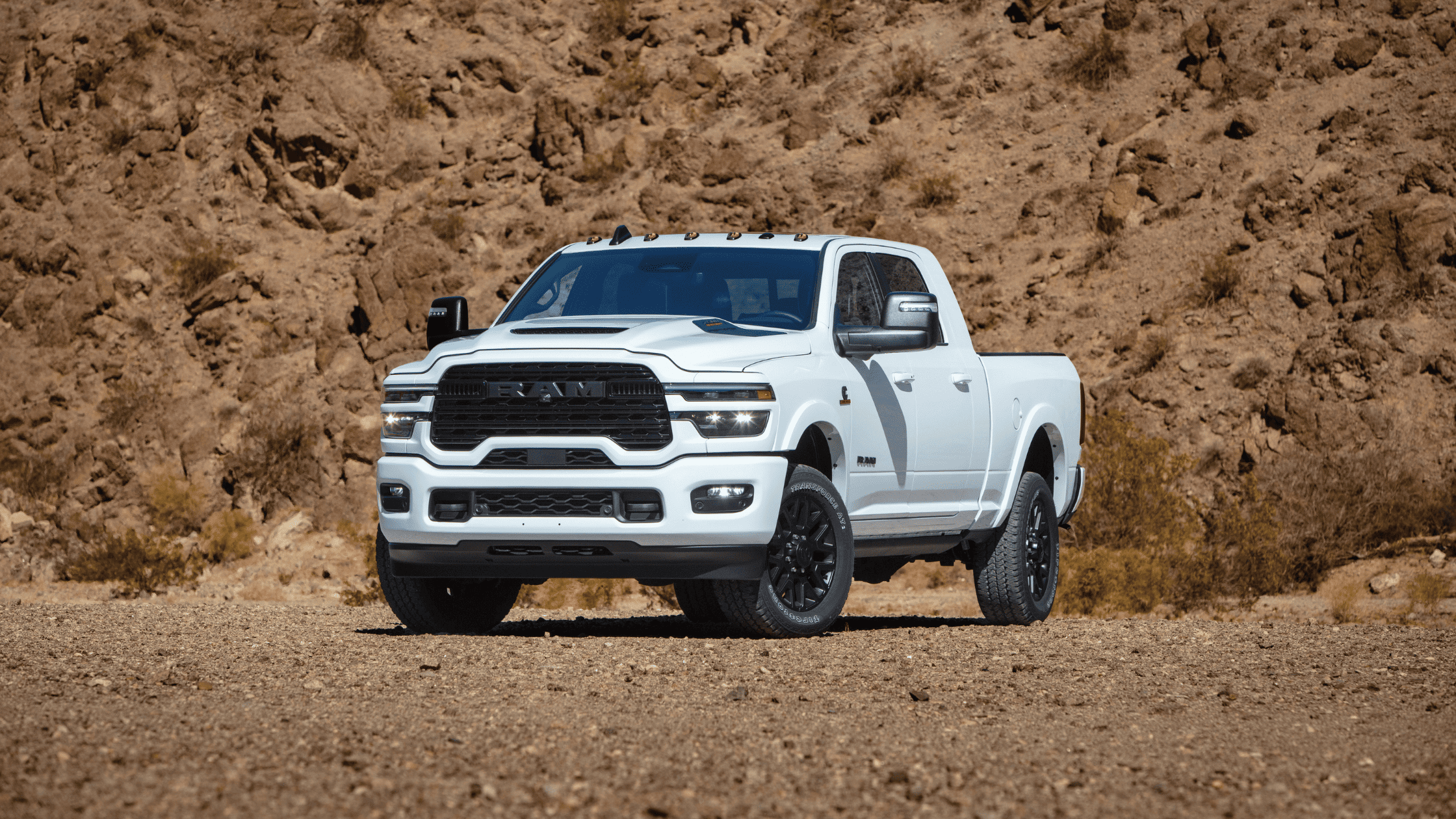 Front-side view of a white 2025 Ram 2500 parked on rocky terrain with blacked-out wheels and grille.