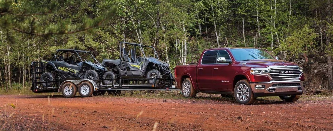 A maroon 2023 Ram 1500 towing ATVs. 