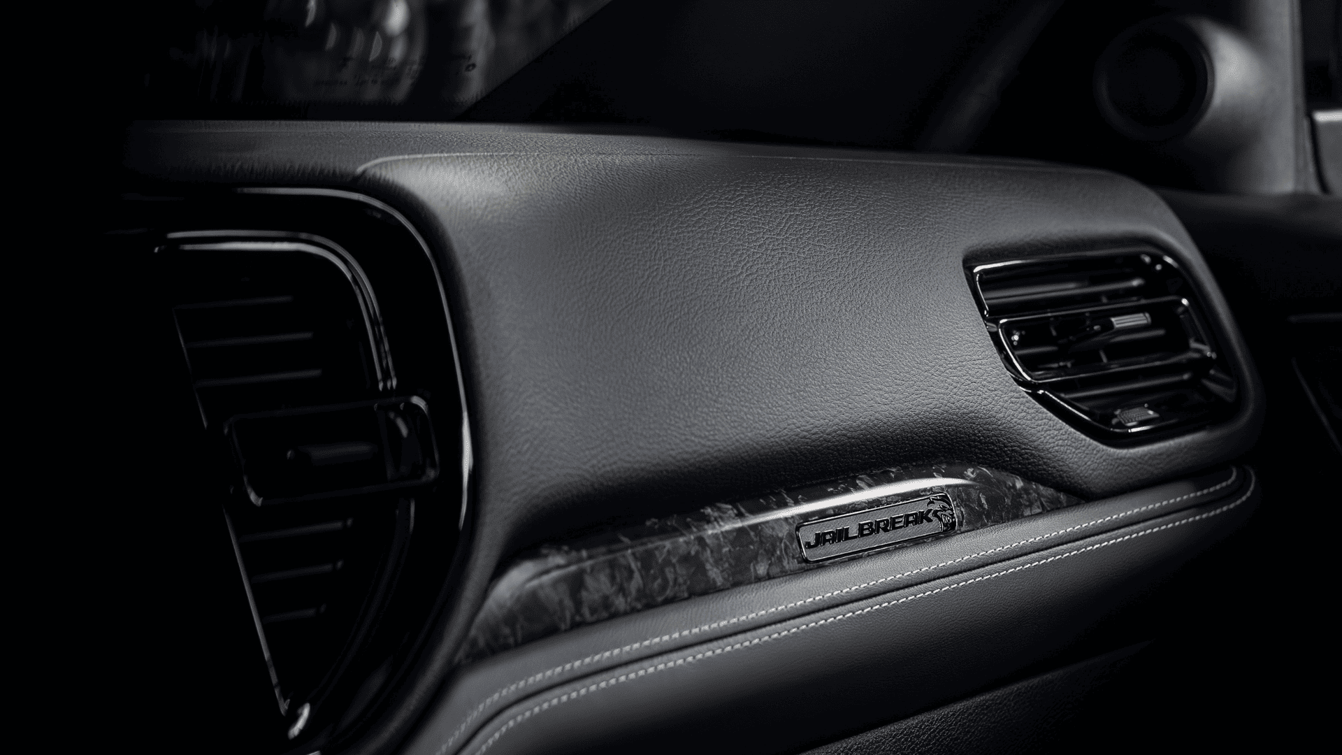 Detail shot of the Jailbreak badge on the dashboard trim of the 2026 Dodge Durango, featuring black leather and carbon fiber accents.