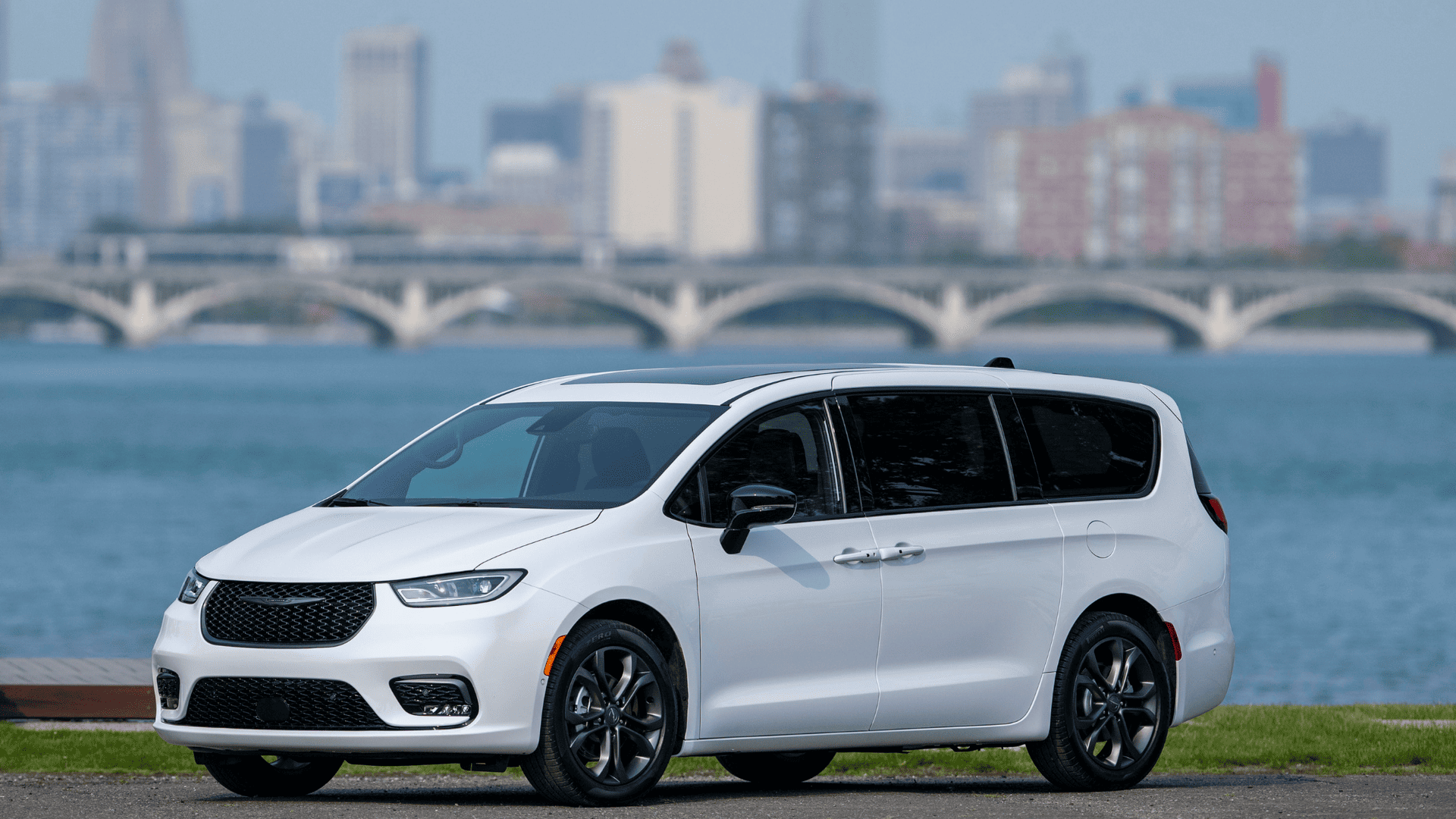 Side view of the 2026 Chrysler Pacifica in white parked near waterfront with city skyline in background.